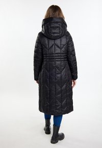 Hosszú fekete pehelykabát, kapucnival, átlós steppelt mintázattal, megkötött derékkal és sima felülettel. Kék leggings-szel és fekete csizmával párosítva.
