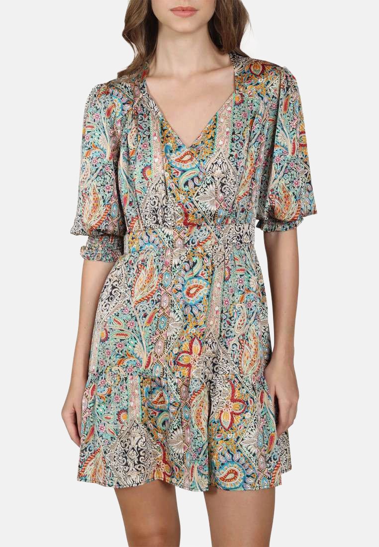 Femme portant une robe portefeuille colorée et à motifs avec des manches bouffantes et un col en V, se tenant devant un fond clair.