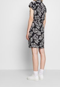 Robe noire à manches courtes avec un motif floral blanc, cintrée à la taille. Portée avec des baskets blanches et des chaussettes montant à la cheville.