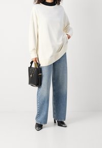 Sweatshirt crema oversize con spalle cadute, abbinato a jeans a gamba larga blu chiaro. Borsa nera strutturata e scarpe con tacco nere a punta con dettagli in argento.