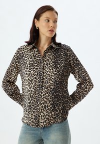 Chemise en mélange de soie avec imprimé léopard ; manches longues, fermeture boutonnée à l'avant, col classique, avec des tonalités noires et beiges, finition subtilement brillante.