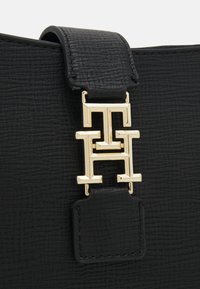 Borsa in pelle nera con texture, caratterizzata da una chiusura logo in metallo dorato di grande impatto, con tracolla liscia e dettagli cuciti.