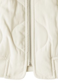 Gequilte crèmekleurige jas met een zilveren rits, ribbels aan de mouwen en een gladde structuur met ronde stikpatronen aan de voorkant.