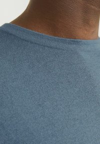 Blauer, gestrickter Rundhalsausschnitt-Pullover mit feiner Textur, Nahaufnahme des Kragens und des Ausschnitts, die die glatte Maschinenstichdetails und die Stoffqualität zeigt.