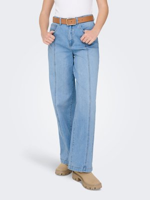 Lyseblå, høytlivs, vide jeans med synlige sømmer. Kombinert med et brunt belte og beige tresko med tykk såle.