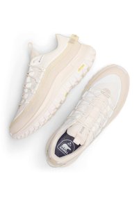 Ljusbeige vandringsskor med ovandel av strukturerat mesh, robust gummisula och minimala gula accenter. Har elastiska snören för en säker passform.