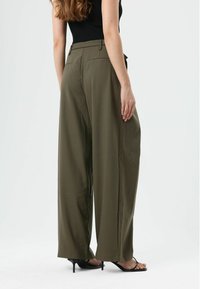 Wijde broekspijpen in olijfgroen stof, met een hoge taille, twee achterzakken en een gladde textuur, gecombineerd met zwarte sandaalhakken met bandjes.