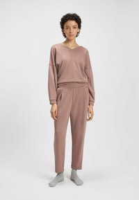 Loungewear set in gedempt roze, met een oversized V-hals top en tapered broek met elastische taille. Zachte stof en casual pasvorm.