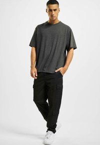 T-shirt grigio a maniche corte con vestibilità comoda, abbinato a pantaloni cargo neri con tasche laterali e sneakers bianche.
