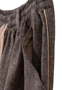 Close-up van donkergrijze, gestructureerde stoffen broek met een elastische tailleband, zijzak en beige bies langs de naad.