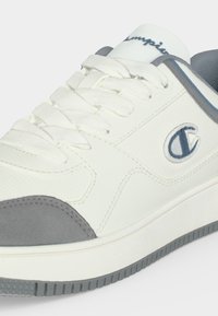 Λευκό και γκρι sneaker χαμηλής κοπής με κορδόνια, υφή στη σόλα και λογότυπο Champion στο πλάι κοντά στη φτέρνα και τη γλώσσα.
