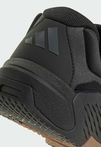 Μαύρο αθλητικό παπούτσι με τακούνι που διαθέτει λαστιχένια σόλα με υφή, λείο μαύρο πάνω μέρος με πλέγμα, και τρεις ανάγλυφες ρίγες λογότυπου σε σκούρο γκρι.