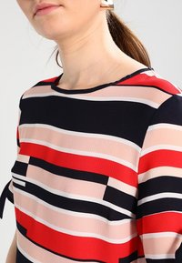Abalorio multicolor con rayas horizontales en rojo, rosa, marino y blanco. Tejido suave con escote redondo y mangas cortas.