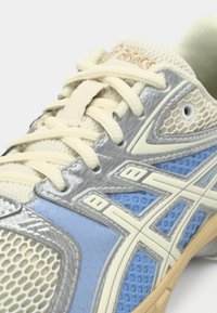 Ténis de corrida em malha azul e cinzenta clara com textura de favo de mel, apresentando atacadores creme e o logótipo destacado da ASICS. Sola de borracha para tração.