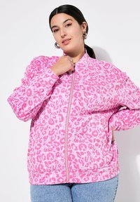 Veste zippée rose avec un motif léopard et des accents roses clairs et foncés. Fabriquée en tissu doux et texturé.