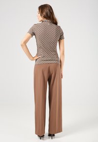 Bruin gemustered overhemd met korte mouwen, gecombineerd met losse bruine broek. Het overhemd heeft een geometrisch ontwerp, terwijl de broek een gladde textuur heeft.