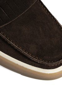 Braunes Wildleder-Slipper mit vertikalen Steppnähten auf dem Obermaterial, creamfarbener Gummisohle und kontrastierenden beigen Akzenten.