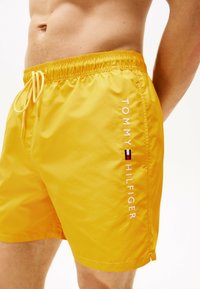 Shorts de bain jaunes en matériau léger, avec une taille élastique, un cordon de serrage et le logo "TOMMY HILFIGER" en blanc.