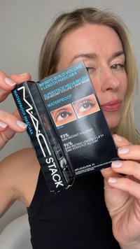 Frau hält die Verpackung der MAC Stack wasserfesten Mascara, auf der Vorher-Nachher-Fotos der Wimpern und Produktversprechen zu sehen sind.