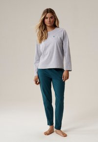 Szara bluzka z długim rękawem z małym zielonym wzorem liścia, w połączeniu z turkusowymi spodniami, obie części o miękkiej fakturze i luźnym kroju.