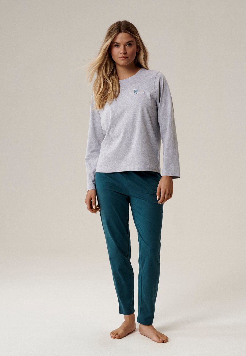 Szara bluzka z długim rękawem z małym zielonym wzorem liścia, w połączeniu z turkusowymi spodniami, obie części o miękkiej fakturze i luźnym kroju.