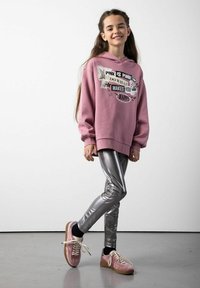 Różowy sweter z grafiką, w zestawieniu z błyszczącymi srebrnymi legginsami i różowymi sneakersami. Gładki materiał z luźnym krojem i długimi rękawami.