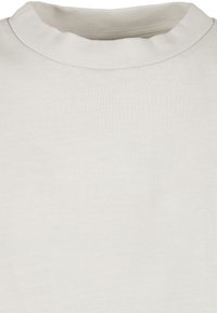 Chemise à manches courtes beige clair avec un col rond côtelé, confectionnée en tissu de coton doux, à la texture lisse et au design minimaliste.