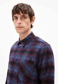 Geruite flanellen overhemd in tinten van blauw, paars en zwart. Voorzien van een knoopsluiting aan de voorkant, een kraag en een borstzak met een gestructureerde afwerking.