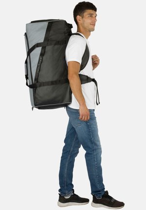 Schwarze und graue Reisetasche mit verstellbaren Riemen, rechteckiger Form, oberen Griffen und deutlich sichtbarem Markennamen.