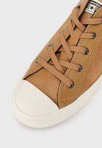 Skórzane sneakersy w kolorze brązowym z białą gumową osłoną na palce, brązowymi sznurowadłami, czarnymi oczkami i teksturowaną powierzchnią. Zawierają naszywkę z logo na języku.