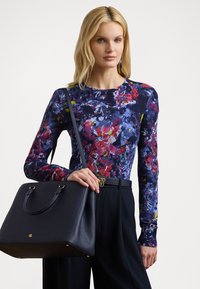 Camisa de manga larga con un patrón floral oscuro en azul, púrpura y rojo, combinada con un bolso estructurado negro con acentos dorados.