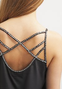Top in satin nero con design incrociato sul retro e dettagli metallici lungo le spalline. Texture liscia, silhouette aderente.
