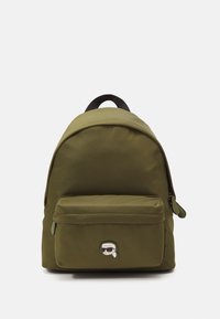 Zaino verde oliva realizzato in materiale tessile, con parte superiore curva, tasca frontale con zip e una toppa con logo di cartone sulla parte anteriore.