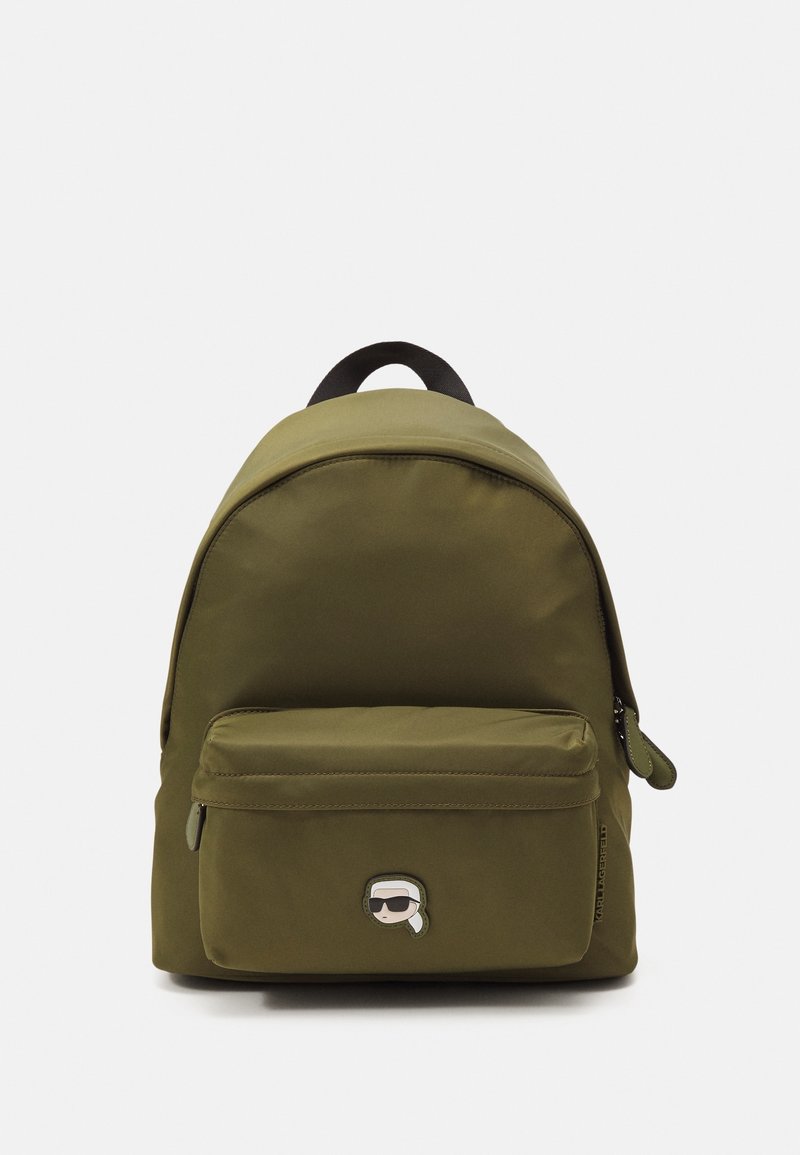 Zaino verde oliva realizzato in materiale tessile, con parte superiore curva, tasca frontale con zip e una toppa con logo di cartone sulla parte anteriore.