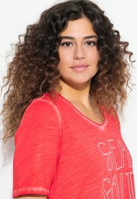 T-shirt corail à col en V avec des manches courtes, présentant un graphisme "SEA SALT" en blanc. Tissu doux avec un aspect légèrement texturé et usé.