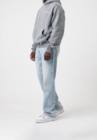 Grå huvtröja med framficka, matchad med ljusblå avslappnade denimjeans och vita sneakers med grå detaljer.