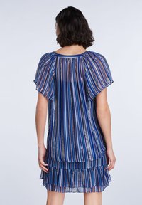 Vestito blu trasparente con strisce in diverse tonalità di blu, oro e argento. Presenta maniche a flutter e un orlo a strati con volant.
