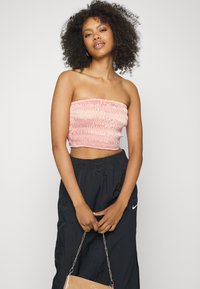 Top cropped sem alças, em rosa, com tecido franzido. Combinado com calças de treino pretas, com cordão na cintura e logotipo da Nike.