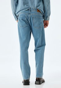 Jeans in denim azzurro chiaro con taglio dritto, dotati di due tasche posteriori e una toppa in pelle vicino alla vita. Tessuto morbido e testurizzato.