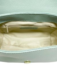 Interior de un bolso de mano de cuero verde claro con un forro beige, que cuenta con un bolsillo con cremallera y un diseño liso y estructurado. Detalle de herrajes dorados visible.