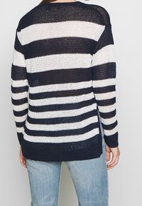 Knitted sweater with navy and white horizontal stripes. Features a loose fit, long sleeves, and side slits, made from a breathable fabric.