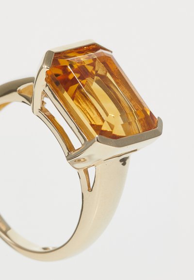 Bague en or ornée d'une grande pierre précieuse en ambre de forme rectangulaire avec des surfaces facettées, présentant une finition polie et des accents ouverts sur l'anneau.