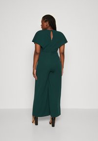 Teal jumpsuit met korte cape mouwen, sleutelgat achterkant en wide-leg ontwerp. Glad materiaal met een getailleerde taille en uitsparingen voor bewegingsgemak.