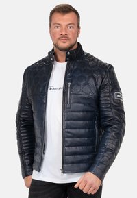 Marine leren jack met hexagonale gestikte structuur, hoge kraag, ritssluiting aan de voorkant en strakke zijzakken. Gemaakt over een wit T-shirt.