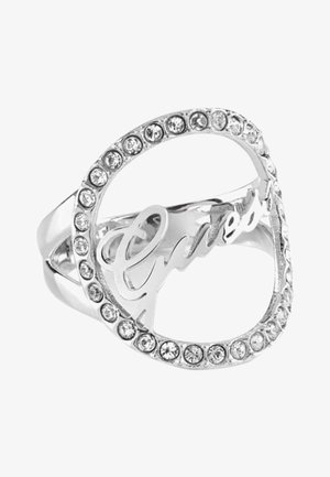 Silberner Ring mit herzförmiger Umrandung, verziert mit kleinen klaren Edelsteinen und dem Schriftzug "Guess" innerhalb des Herzens.