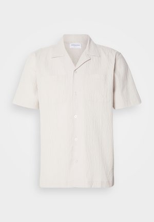 Short-sleeved, light beige shirt with a textured fabric, notched collar, and two chest pockets, featuring a button front closure.