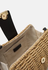 Tkaná slámová kabelka s béžovým lněným interiérem. Obsahuje černé kožené rukojeti a uzávěr ve zlatém tónu. Jednoduchý a funkční design.