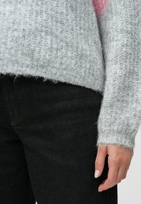 Pelēks adīts džemperis ar teksturētu apdari, kuram ir platas piedurkņu malas. Saskaņots ar melnām džinsa biksēm, kas izceļ relaksētu piegriezumu.