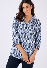 Blusa blu con motivo che presenta una combinazione di forme in blu navy, azzurro e bianco. Maniche lunghe con bottone e scollo rotondo.