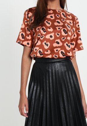 Femme portant un haut à manches courtes imprimé léopard de couleur rouille, rentré dans une jupe plissée noire taille haute.